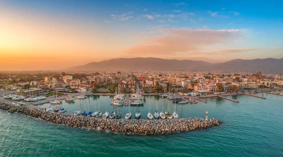 Aerial view of Kalamata marina at sunset with sailboats moored along the breakwater and the city in the background
